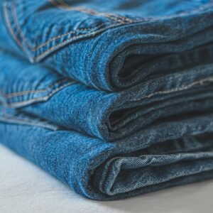Stack of neatly folded blue denim jeans showcasing texture and stitching.